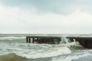Karadeniz 'deki eski bir beton iskelede. İskelenin taştan tabanı dalgalarda ve okyanusta köpükler bulutlu havada. Georgia 'daki Magnetiti Ureki sahilinde yıkılmış bir iskele.