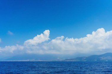 Güneşli bir yaz gününde Türkiye 'de Akdeniz' e giden bir tekneden Antalya kıyı manzarası. Deniz ve dağlar bulutlarla ve mavi gökyüzüyle