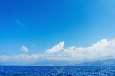 Güneşli bir yaz gününde Türkiye 'de Akdeniz' e giden bir tekneden Antalya kıyı manzarası. Deniz ve dağlar bulutlarla ve mavi gökyüzüyle
