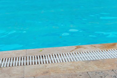 The edge of the home pool with blue water. Cleaning system with plastic protection on the pool