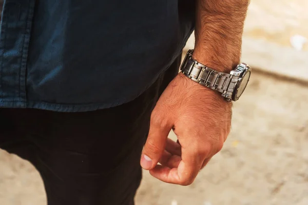 a man with a mechanical watch on his hand. guy in a blue t-shirt with a watch on his wrist. iron strap on men\'s watch