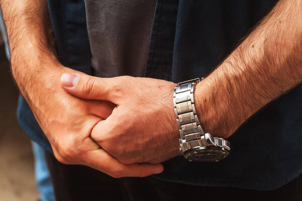 a man with a mechanical watch on his hand. guy in a blue t-shirt with a watch on his wrist. iron strap on men's watch