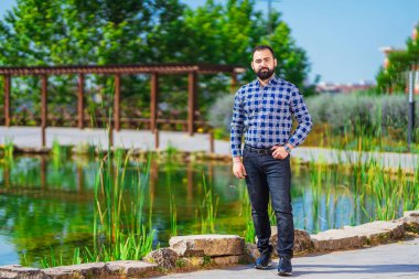 Sakallı bir adam gölün yanındaki parkta duruyor. Türkmen parkta dinleniyor. Parktaki bir ofis çalışanının fotoğraf çekimi.