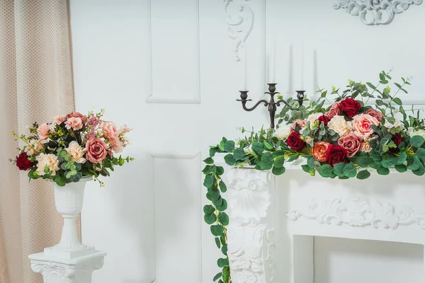 white fireplace in a classic bright room. decorative plaster fireplace in a photo studio with flowers. candlesticks for candles on the fireplace with plastic flowers