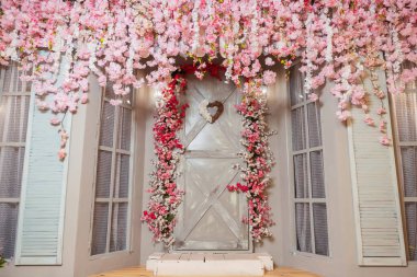 Gri kapısı ve pembe çiçekleri olan bir veranda. Fotoğraf stüdyosunda pembe sakura çiçekleri olan bir fotoğraf bölgesi. Evin dekoratif girişi mobilyalı ve kapısı olan..