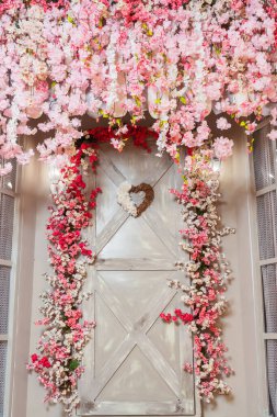 Gri kapısı ve pembe çiçekleri olan bir veranda. Fotoğraf stüdyosunda pembe sakura çiçekleri olan bir fotoğraf bölgesi. Evin dekoratif girişi mobilyalı ve kapısı olan..
