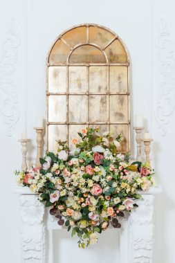 Çiçekleri ve altın aynası olan beyaz şömine. Şöminesi ve yapay çiçekleri olan parlak klasik bir oda. Fotoğraf stüdyosunda fotoğraf çekimi için fotoğraf bölgesi.