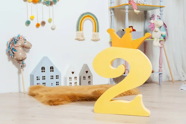 number two in the children's room. number two from polystyrene against the background of toys and a wooden house in the room of a small child. light photo zone with a number in a photo studio