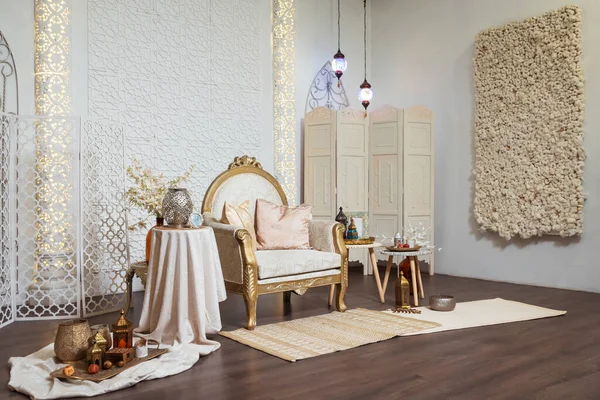 light armchair with tables in oriental style. oriental photo zone in a photo studio with lamps and fabrics. photo zone in Arabic style with carpets and flowers