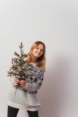 Geyik ve elinde Noel ağacı olan örgü kazaklı bir kız. Örgü örülmüş yeni yıl kazağında, ışık duvarında hayvanlar olan Slav bir kız. Yılbaşı fotoğraf çekimi için bir kadının üzerinde Noel süveteri