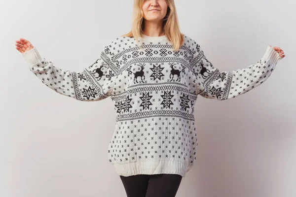 girl in a knitted sweater with deer. Slav girl in a knitted New Year\'s pullover with animals on a light wall. Christmas sweater on a woman for a New Year\'s photo shoot