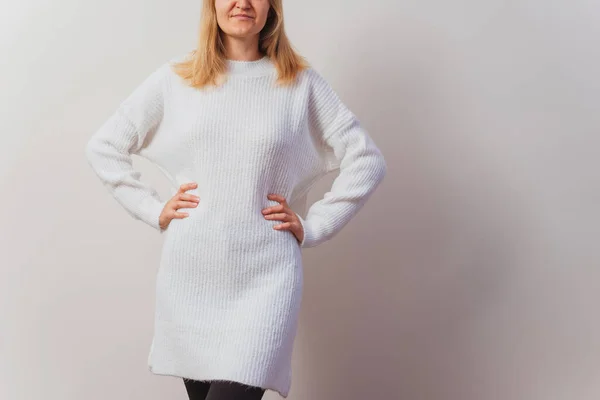 girl in a knitted dress on a white wall. hand-knitted long sweater for New Year\'s Eve. Russian girl in a light knitted pullover