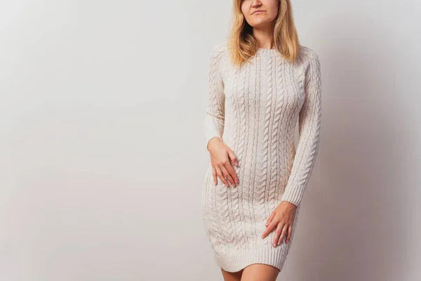 girl in a knitted dress on a white wall. hand-knitted long sweater for New Year\'s Eve. Russian girl in a light knitted pullover