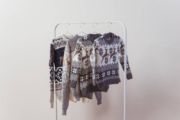 knitted sweaters for christmas on a white metal hanger in the room. several jumpers for the new year are displayed on iron hangers. New Year's photo shoot clothes