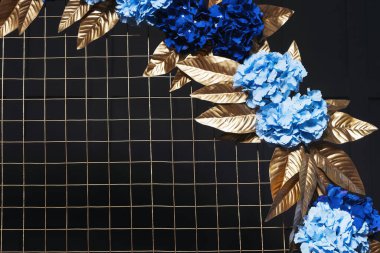 Metal kemerde mavi çiçekli altın yapraklar. Bir fotoğraf stüdyosundaki siyah duvarın arka planında çiçekler olan altın kemer. İç mekanda düğün fotoğrafı ayrıntıları