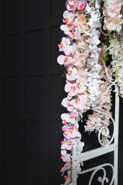 Fotoğraf bölgesinde suni çiçekli beyaz metal kemer. Siyah bir arka planda, düğün fotoğrafında beyaz çiçekler. Yapay çiçekli bir düğün fotoğrafı çekimi için hazır fotoğraf bölgesi.