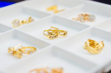 Altın mücevherli sergi tepsisi. Altın yüzüklü ve küpeli küçük hücreler bir insana satılıyor. Mücevher için bölmeleri olan beyaz plastik bir kutu. Katalog için altın mücevher fotoğrafları