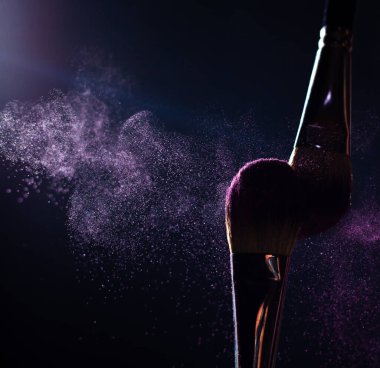 Koyu arkaplanda pembe ya da menekşe tozlu makyaj fırçaları