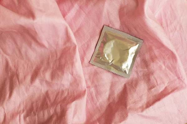 Preservativo su stropicciato il lenzuolo rosa — Foto Stock