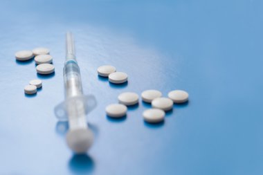 Mavi arka planda şırınga ve haplar