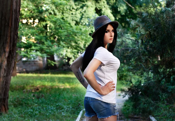 Beautiful young girl with a tattoo in hat and shorts — Stock Photo, Image