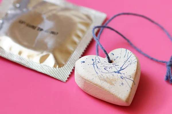 Coração e um preservativo no fundo rosa close up — Fotografia de Stock