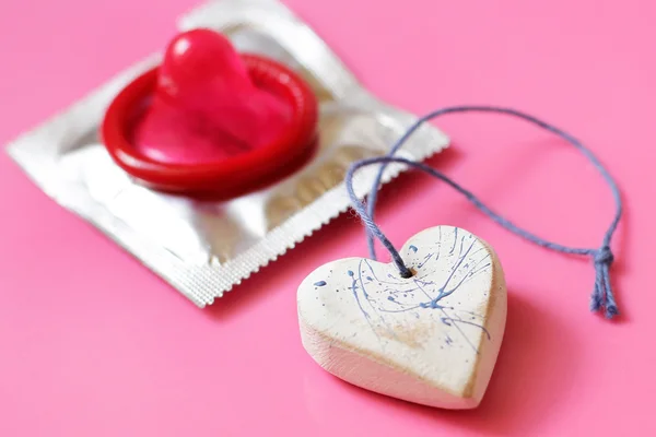 Herz und rotes Kondom auf rosa Hintergrund in Nahaufnahme — Stockfoto