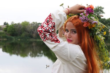 Uzun kızıl saçlı, mavi gözlü, beyaz ve kırmızı işlemeli kırmızı elbiseli güzel bir Slav kız. Ivan Kupala ziyafeti