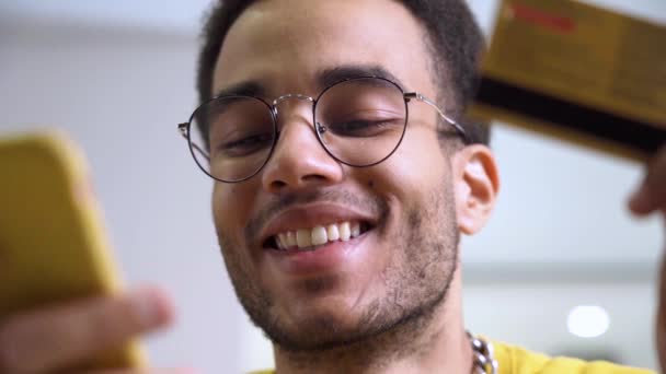 Um jovem afro-americano sorridente com cartão de crédito e smartphone. — Vídeo de Stock