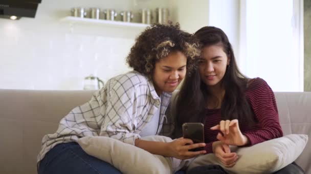 Glückliche Freundinnen schauen aufs Smartphone, sitzen zu Hause zusammen auf der Couch — Stockvideo