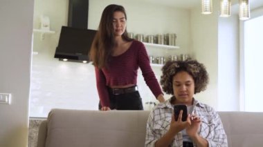 Ağır çekim: İki kız arkadaş, bir Afro-Amerikalı ve bir Asyalı, kanepede otururken birbirleriyle sohbet ediyorlar.