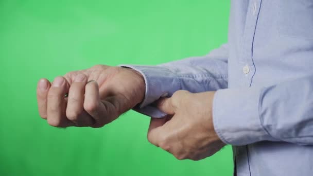 Egy idős férfi kezei, amint gombolja a gombot az ingujján, zöld alapon. — Stock videók