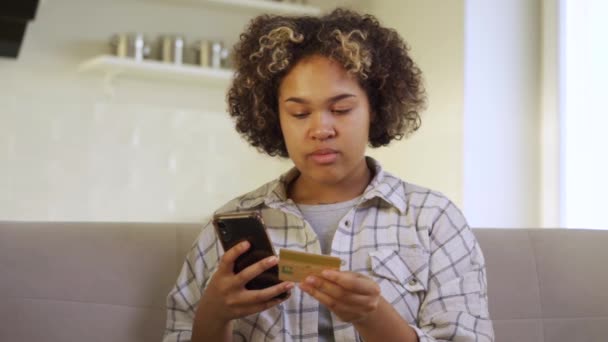 Eine junge Afroamerikanerin bezahlt zu Hause mit ihrem Smartphone — Stockvideo