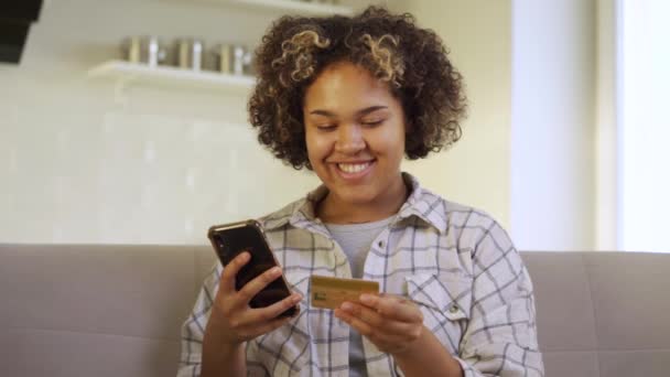 Μια ευτυχισμένη νεαρή Αφρο-Αμερικανίδα πληρώνει μέσω του smartphone της στο σπίτι — Αρχείο Βίντεο