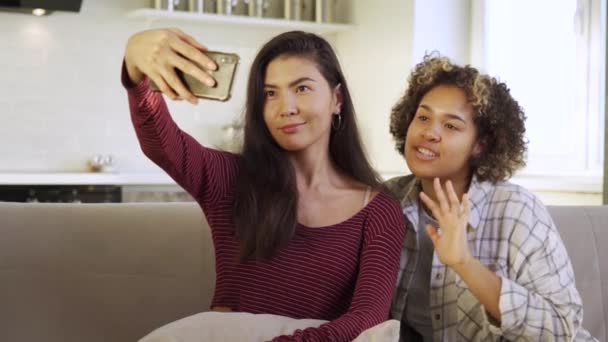 Happy young two girlfriends, an African-American and an Asian, take selfies in their house — Stock Video