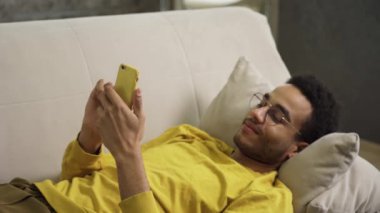 Genç Afrikalı. Akıllı telefon kullanarak koltukta yatıyor.