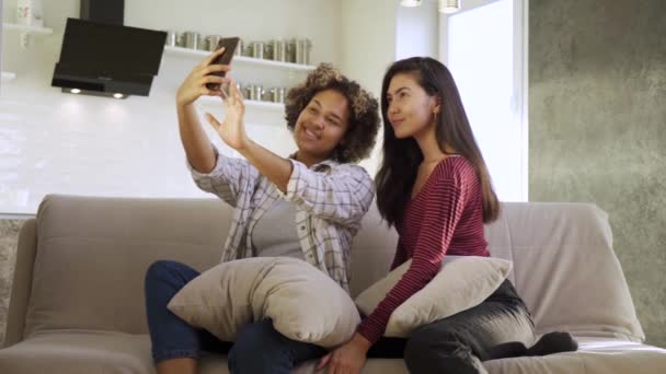 Happy young two girlfriends, an African-American and an Asian, take selfies in their house — Stock Video
