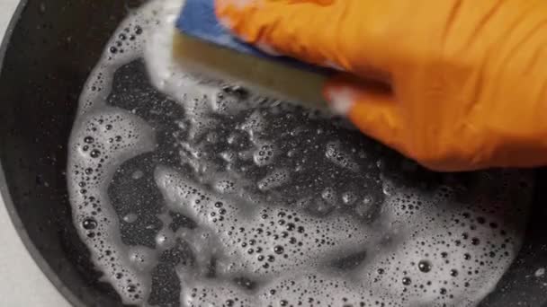 Umyjte pánev houbou a čisticím prostředkem. Ruka v rukavici s houbou myje špinavou pánev. — Stock video