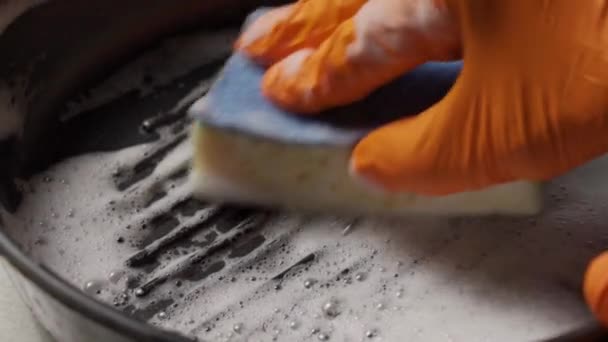 Umyjte pánev houbou a čisticím prostředkem. Ruka v rukavici s houbou myje špinavou pánev. — Stock video