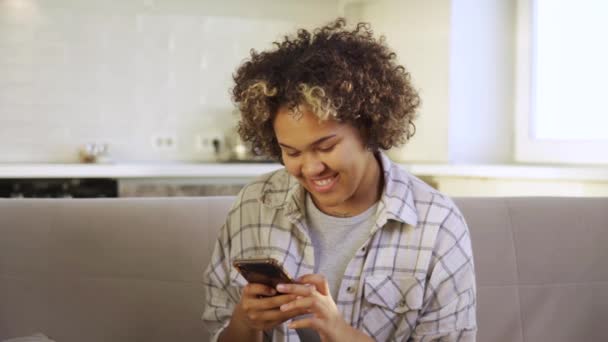 Une jeune Africaine heureuse souriante, lisant et textant sur son smartphone — Video