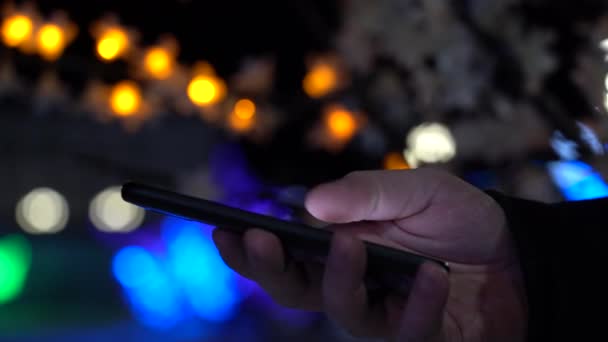 車のブリュリーライトの背景に夜市内のスマートフォンを持つ男の手 — ストック動画
