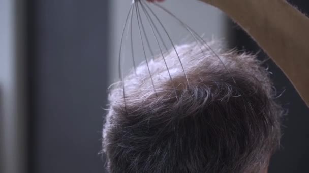 Egy férfi a saját fejbőrét masszírozza egy skalpmasszírozóval. — Stock videók