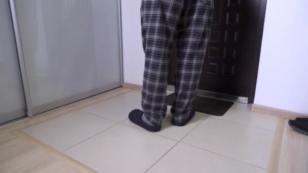 Muž v pantoflích a pyžamu otevře přední dveře a zvedne velkou lepenkovou krabici. — Stock video