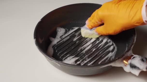 Una mano enguantada con una esponja de espuma lava una sartén sucia en la mesa. — Vídeos de Stock