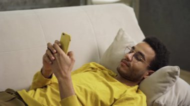 Genç Afrikalı. Akıllı telefon kullanarak koltukta yatıyor.