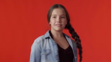 Kameraya bakarken uzun örgülü gülümseyen beyaz bir genç kız.
