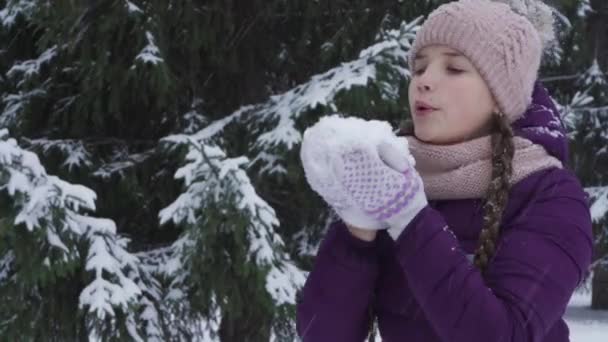 Ein fröhliches Teenager-Mädchen bläst in den Schnee und hat Spaß in einem Winterpark — Stockvideo