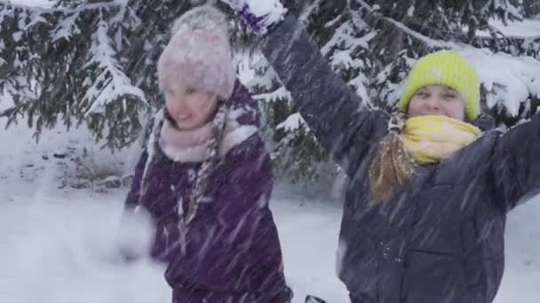 Två tonårstjejer knäböjer i snön och har kul med att kasta snöbollar. Vinternöje — Stockvideo