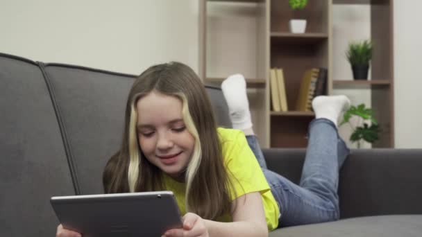 En lycklig vit tonårstjej i en skön soffa som tittar på en film på sin surfplatta — Stockvideo