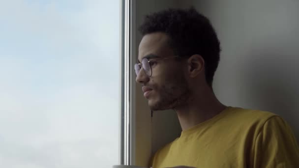 Молодий чоловік в окулярах п'є гарячий напій біля вікна — стокове відео
